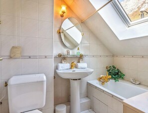 A modern bathroom with a skylight, a pedestal sink, a bathtub, and a toilet.