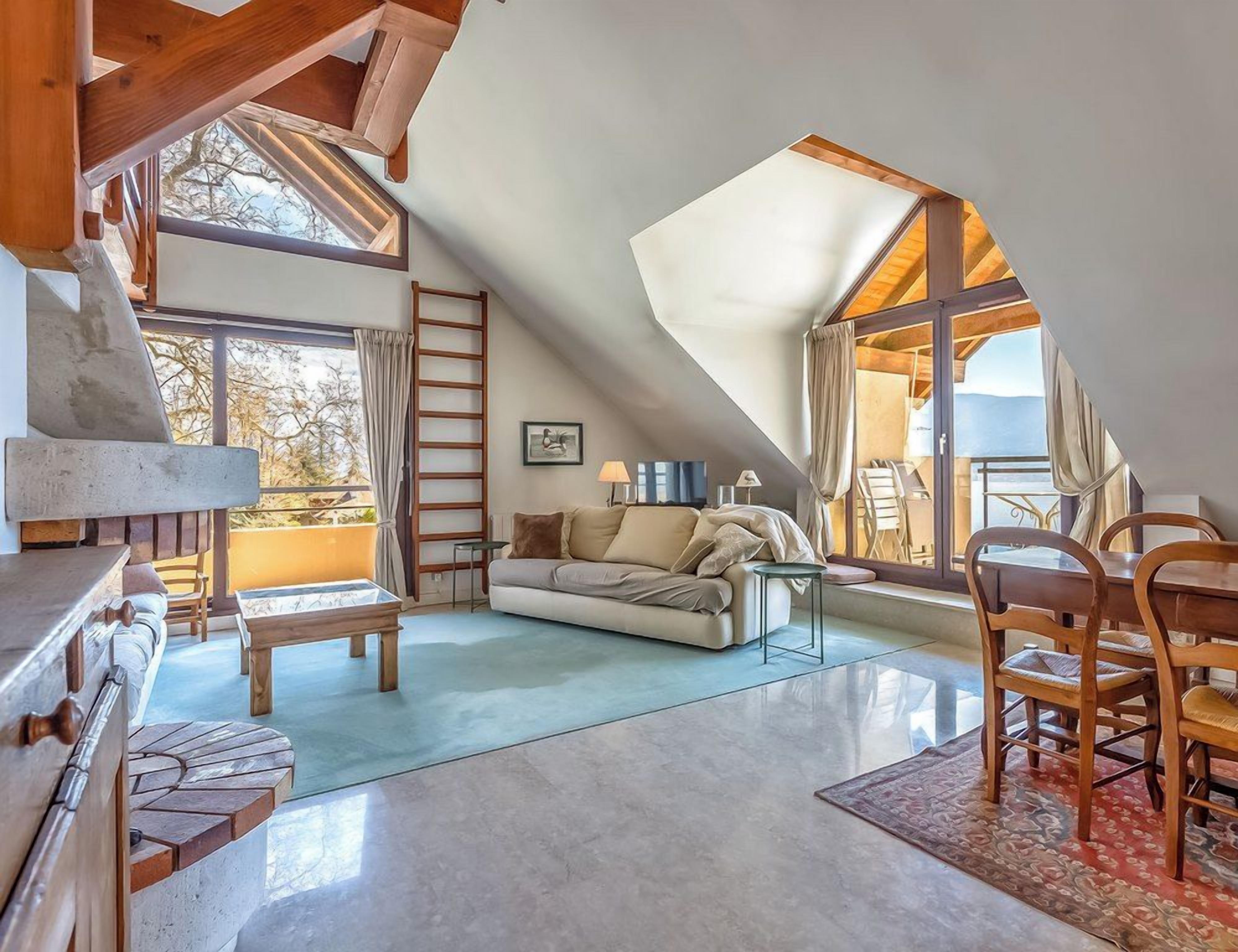 A cozy loft bedroom with a sloped ceiling, a wooden dining table, and a sofa.