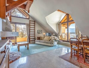 A cozy loft bedroom with a sloped ceiling, a wooden dining table, and a sofa.