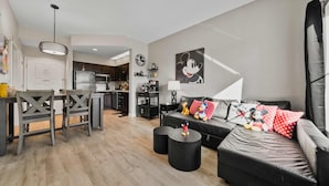 Ein modernes Wohnzimmer mit einer schwarzen Ledersofa, einem Esstisch mit Stühlen und einer Küche im Hintergrund.