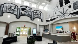 Eine geräumige Lobby mit hoher Decke, einem Empfangsbereich, Sitzgelegenheiten und einem großen Wandbild.