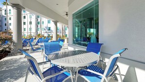 Ein überdachter Außenbereich mit blauen Stühlen und einem runden Tisch mit Blick auf einen Pool und Gebäude.