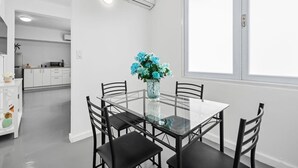 A modern dining area with a glass table and black chairs, a vase with blue flowers, and a kitchen in the background. - Modern Apartment Near Condado Beach with Balcony (San Juan)