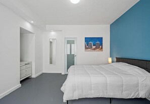 A bedroom with a bed, a dresser, a door, and a painting on the wall. - Condado 3BR for 8 | King Bed | Walk to Beach (San Juan)