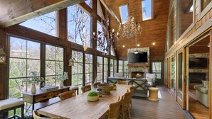 Una amplia terraza de madera con una gran mesa de comedor, sillas de mimbre y una chimenea de piedra.