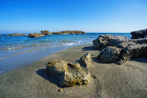 Ein Strand mit klarem Wasser, Kies und Felsformationen.
