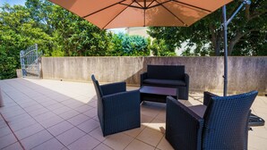 An outdoor patio with a table and chairs under a large umbrella, surrounded by a stone wall and greenery.