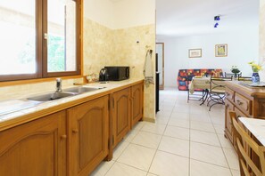 A kitchen with wooden cabinets, a sink, a microwave, and a dining area with a table and chairs. - 2-Bedroom Apartment 100m from the Beach - Private Terrace - Fiber Wi-Fi - A/C (Linguizzetta)