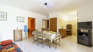 A living room with a sofa, a dining table with chairs, a TV, and a cabinet.