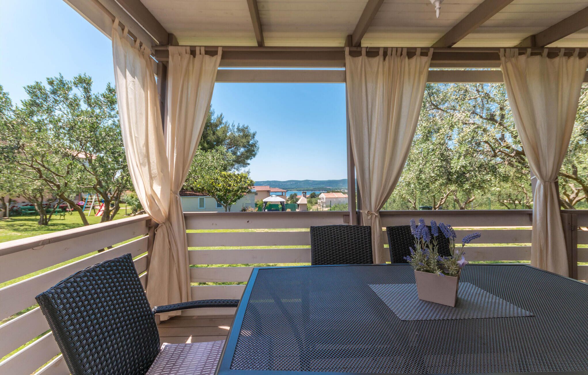 A covered outdoor seating area with a table and chairs, overlooking a residential neighborhood and a distant view.