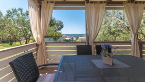 A covered outdoor seating area with a table and chairs, overlooking a residential neighborhood and a distant view.