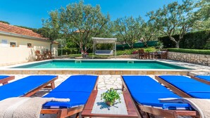 A pool area with lounge chairs, a pergola, and a small garden.