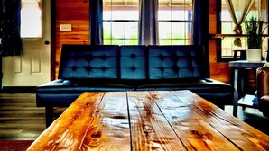 Une table en bois se trouve dans une pièce où il y a un canapé noir et une fenêtre avec des rideaux.