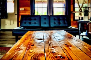 A wooden table in a room with a black sofa and a window with curtains.