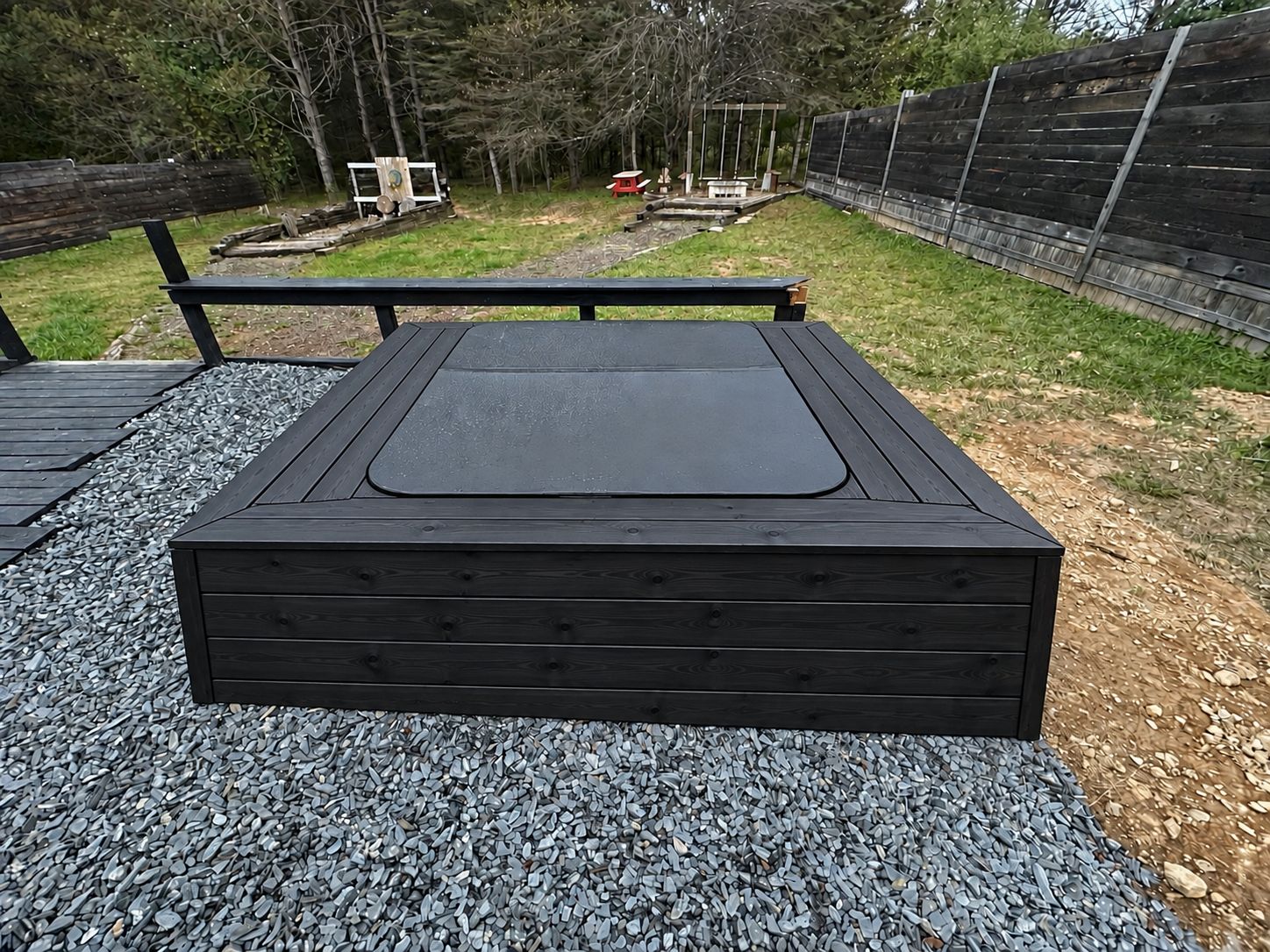 Un espacio de estar al aire libre rectangular con superficie plana, rodeado de grava y una valla de madera.