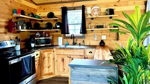 A wooden cabin-style kitchen with built-in appliances, wooden shelves, and a large window. - Mossy at Forest Villas: Private Axe Pit, Swing Fire Pit & Pergola Retreat (Marienville)