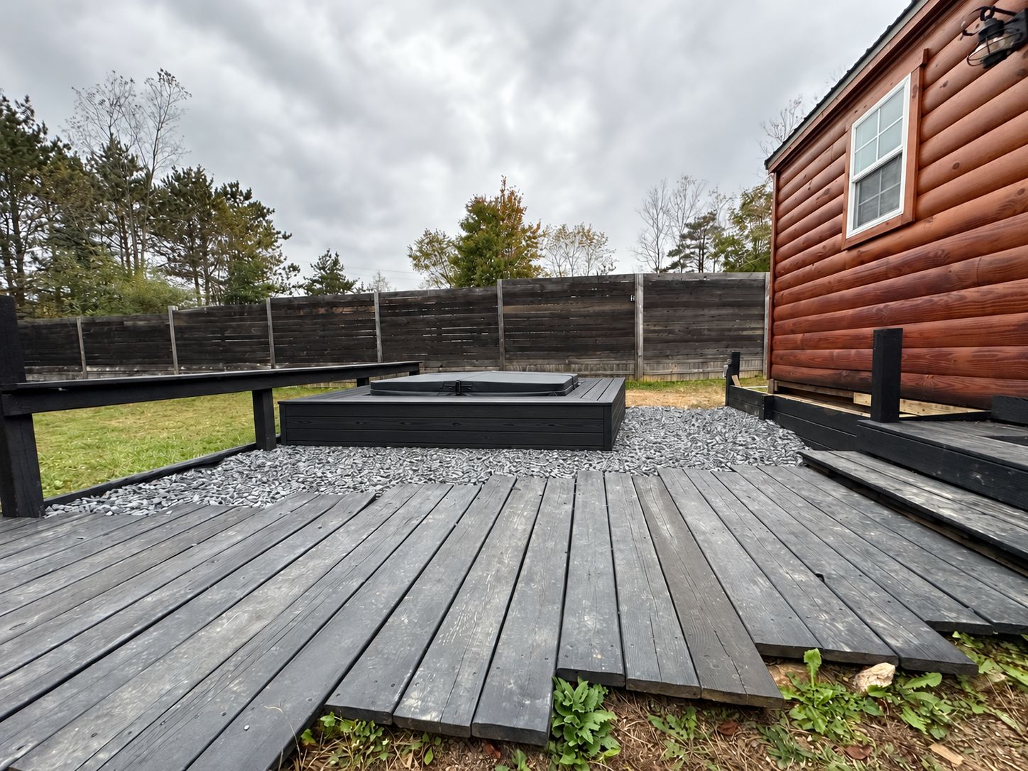 Eine Holzterrasse mit integriertem Whirlpool und einem Holzzaun im Hintergrund.