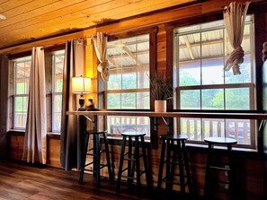 A wooden interior with a bar area, large windows, and a hanging plant. - Mossy at Forest Villas: Private Axe Pit, Swing Fire Pit & Pergola Retreat (Marienville)
