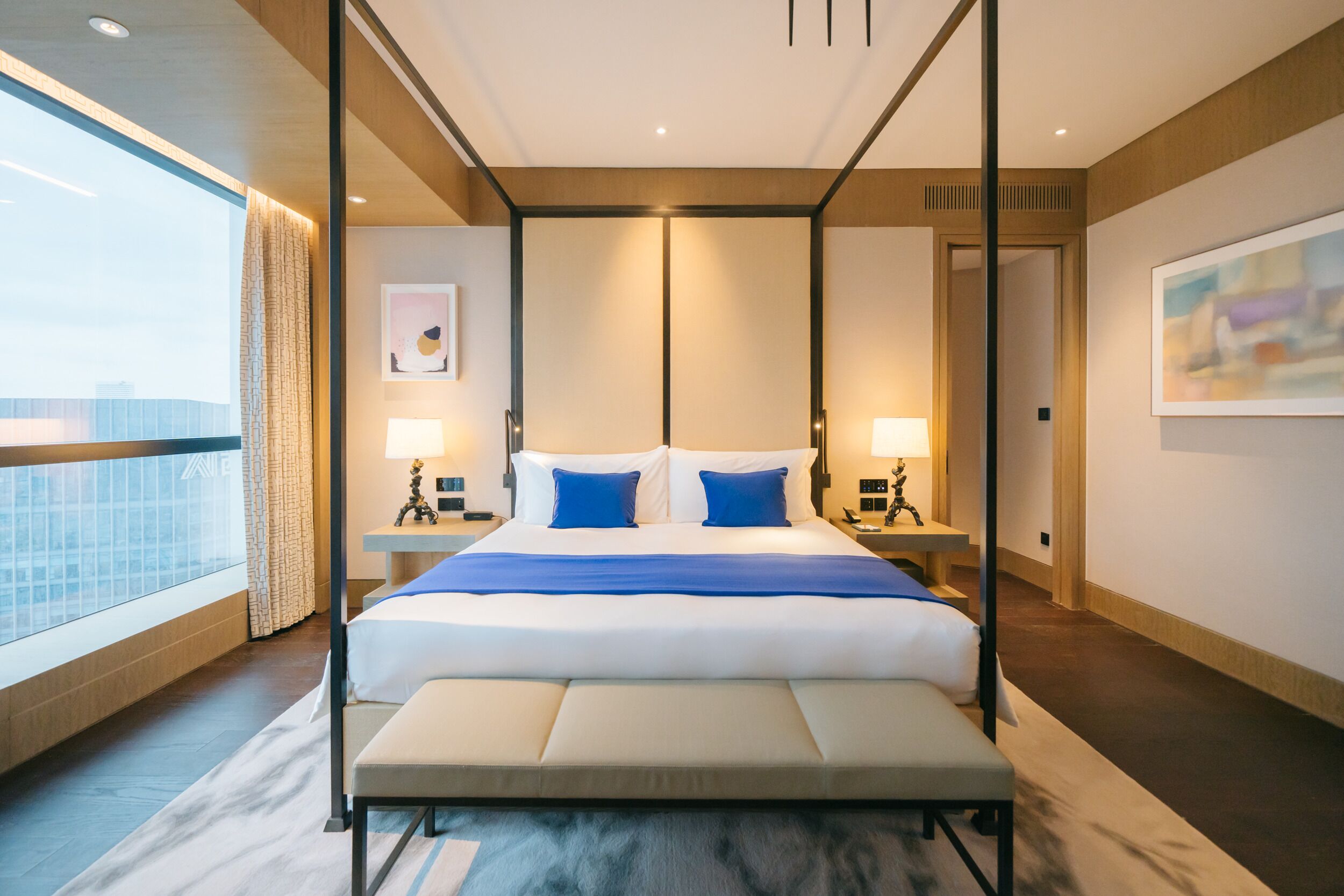 Una habitación de hotel moderna con una cama grande, mesitas de noche y vistas a la ciudad.