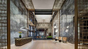 Un'ampia hall con un design moderno, caratterizzata da un'area salotto centrale, una reception e una scala che conduce ai piani superiori.
