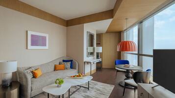 Quarto de hotel moderno com sofá, mesa de jantar, pequena cozinha e janelas amplas.
