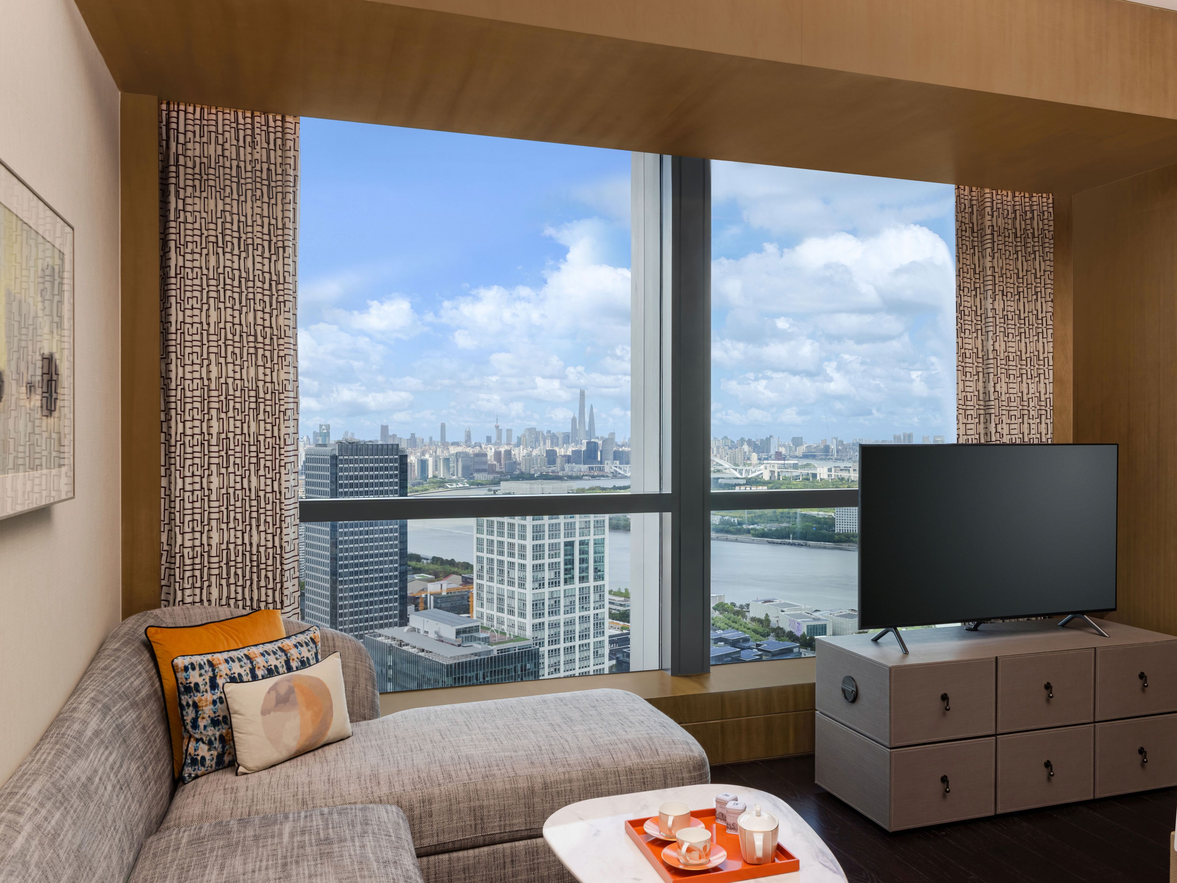 A modern living room with a large window, a flat-screen TV, a sofa, a coffee table, and a cabinet.