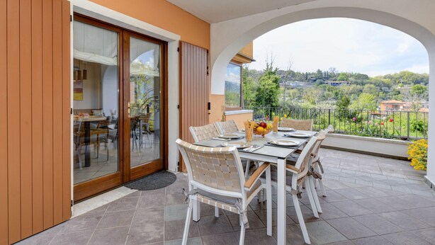 Un balcón con una mesa y sillas de comedor, vista a un pueblo, y una puerta de madera.