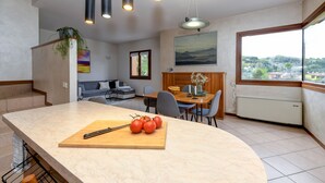 Una cocina moderna con encimera de mármol, comedor con mesa y sillas, sofá y un amplio ventanal con vistas a la ciudad.