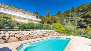 A swimming pool with a stone wall and a view of a building with balconies. - EZE VISTA AP4328 By Riviera Holiday Homes (Eze)