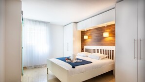 A modern bedroom with a bed, white wardrobe, and a wooden accent wall. - EZE VISTA AP4328 By Riviera Holiday Homes (Eze)