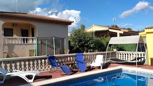 A swimming pool with lounge chairs, a covered seating area, and a building with a tiled roof. - Cozy villa with large private pool and complete barbecue (El Mirador del Penedès)