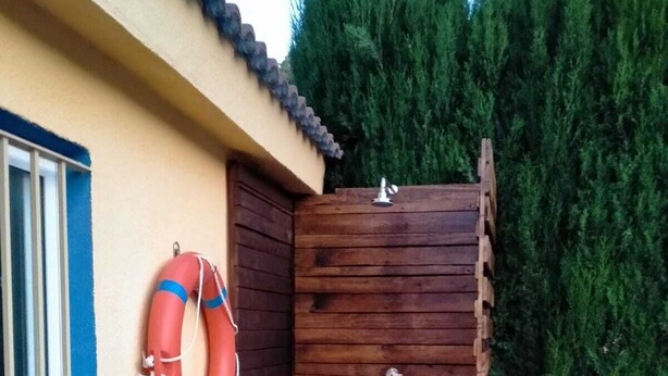 A wooden outdoor shower area with a lifebuoy hanging on the wall, a window with blue trim, and a wooden bench. - Cozy villa with large private pool and complete barbecue (El Mirador del Penedès)