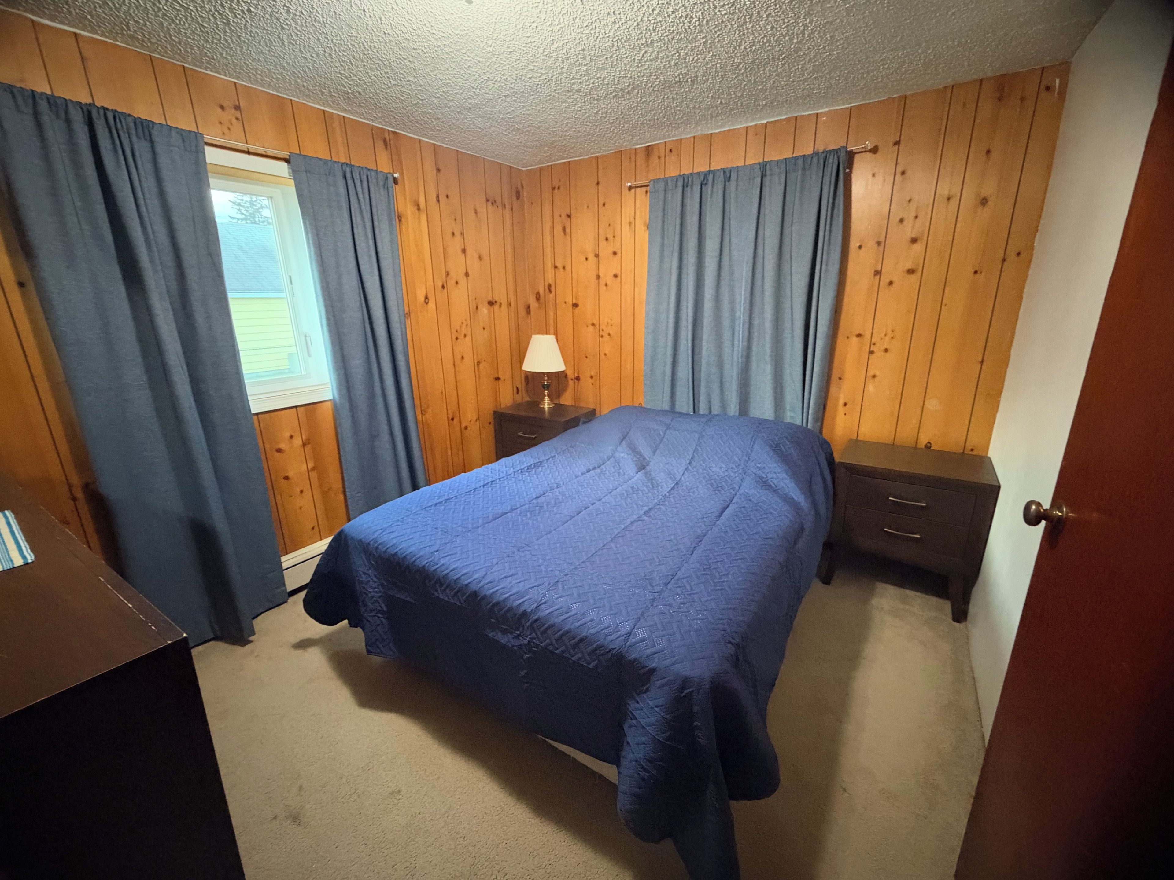Un dormitorio con una cama, dos mesitas de noche, una lámpara y paneles de madera en las paredes.