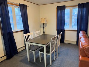 A dining area with a table and chairs, a lamp, and a view through the windows.
