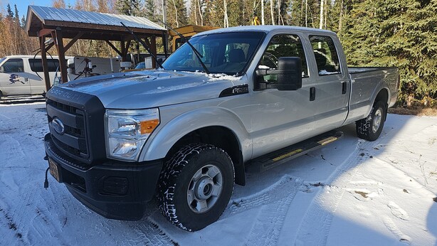 Een zilveren Ford F-350 pick-up truck geparkeerd in een besneeuwd gebied, met een overdekte constructie op de achtergrond.