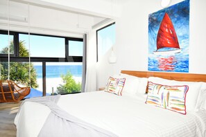 A bedroom with a large bed, a view of the beach, and a painting of a sailboat.