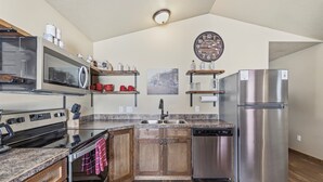 A kitchen with a stainless steel refrigerator, a microwave, and a stove. There are wooden cabinets and a wooden countertop. - Family-Friendly Old West Cabin Near YNP (Island Park)