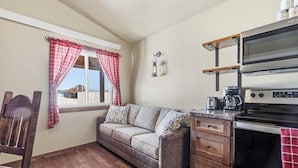 A cozy kitchen with a sofa, wooden chair, and a window with plaid curtains. - Family-Friendly Old West Cabin Near YNP (Island Park)