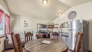 A compact kitchen with a microwave, oven, and refrigerator. There is a dining table with chairs and a clock on the wall. - Family-Friendly Old West Cabin Near YNP (Island Park)