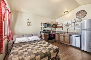 A compact room with a bed, kitchenette, and a clock on the wall.