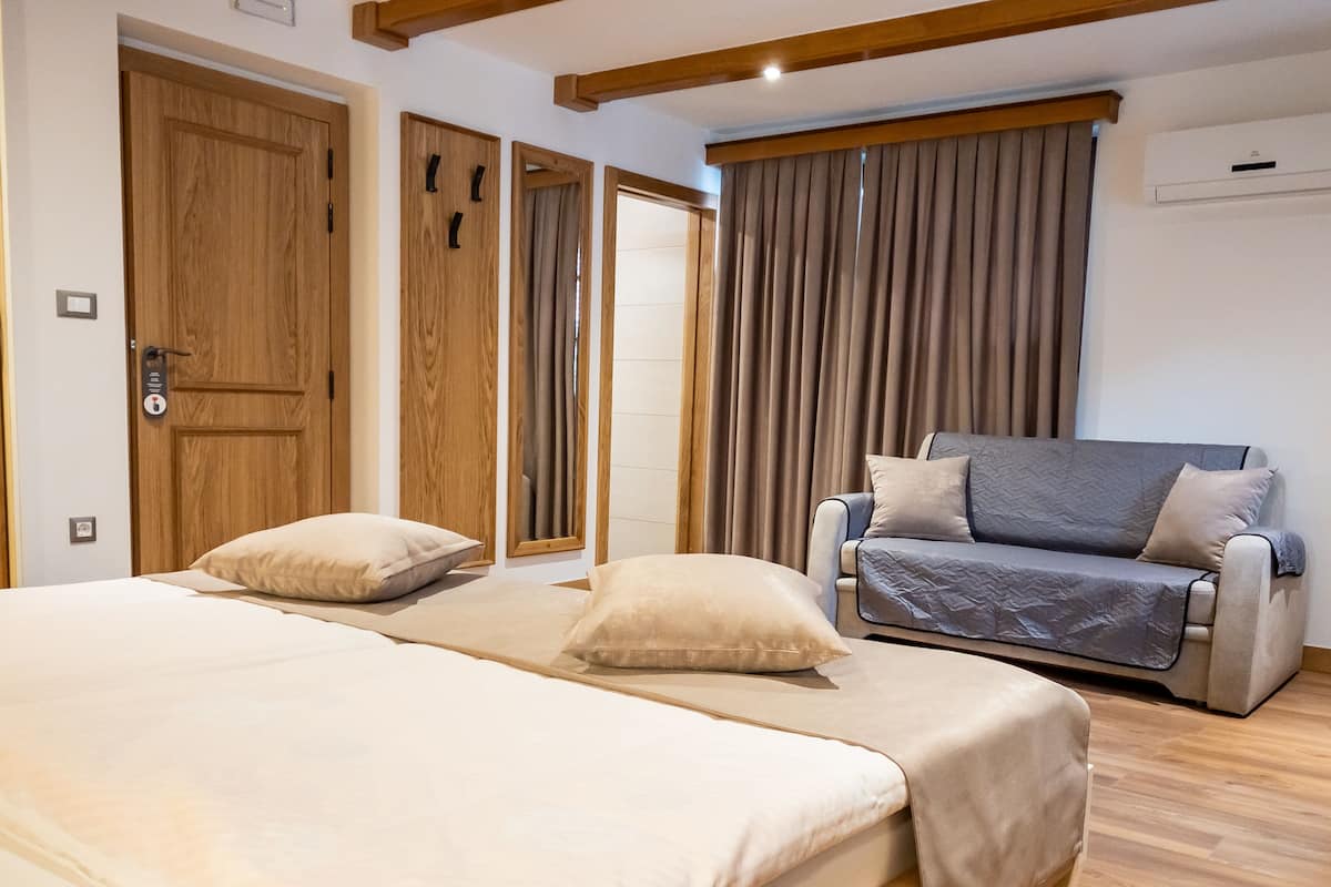 A bedroom with two beds, a sofa, wooden doors, and a window with curtains.