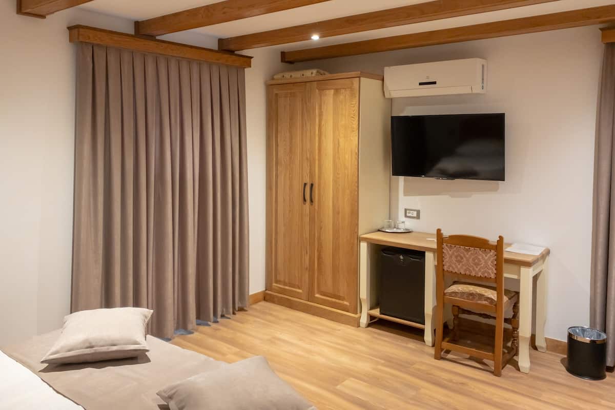 A room with a bed, a desk with a chair, a wardrobe, and a TV mounted on the wall.