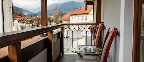 Een balkon met een glazen tafel en een houten stoel, met uitzicht op een stad en bergen op de achtergrond.