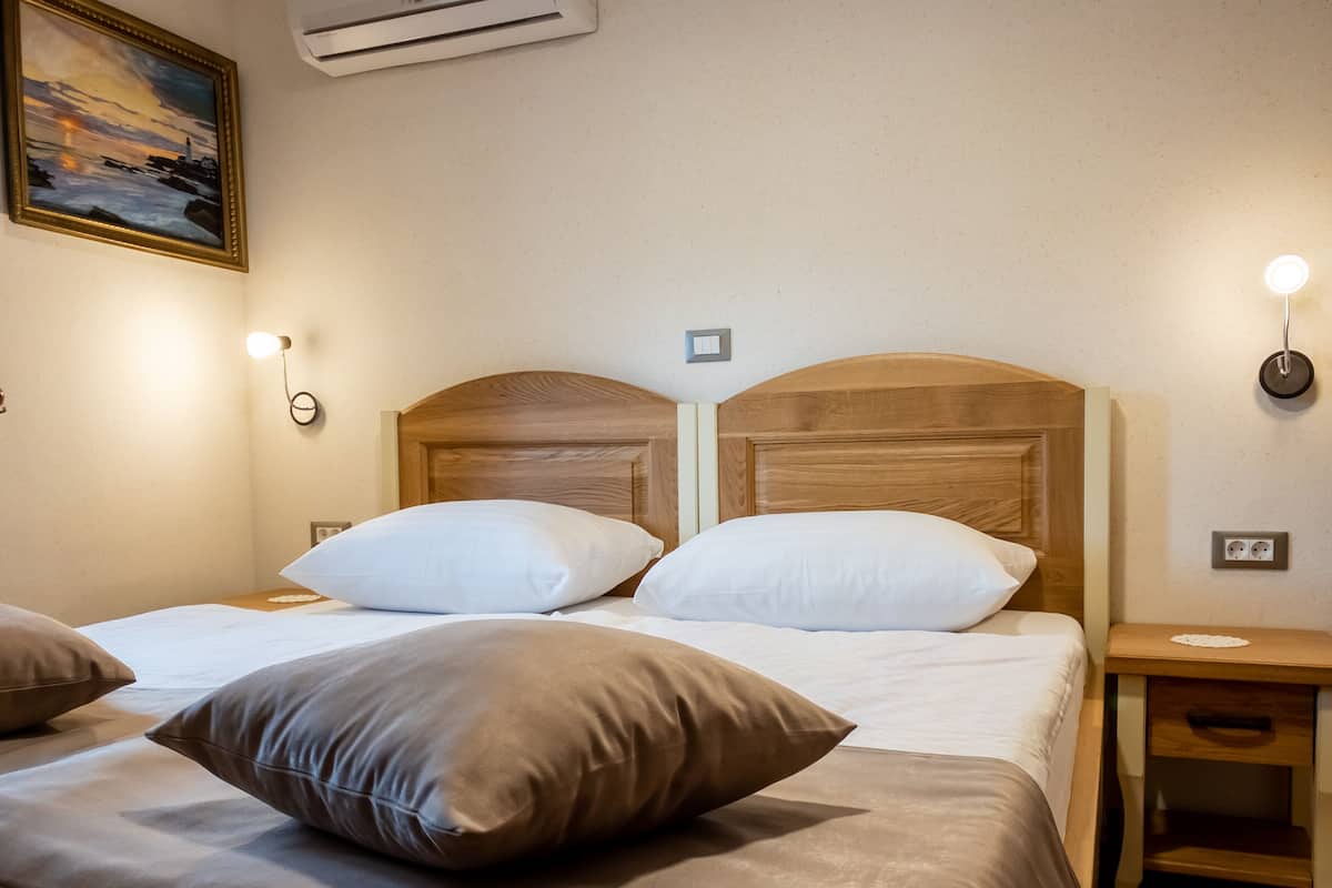 A hotel room with a wooden headboard bed, white bedding, and a painting on the wall.