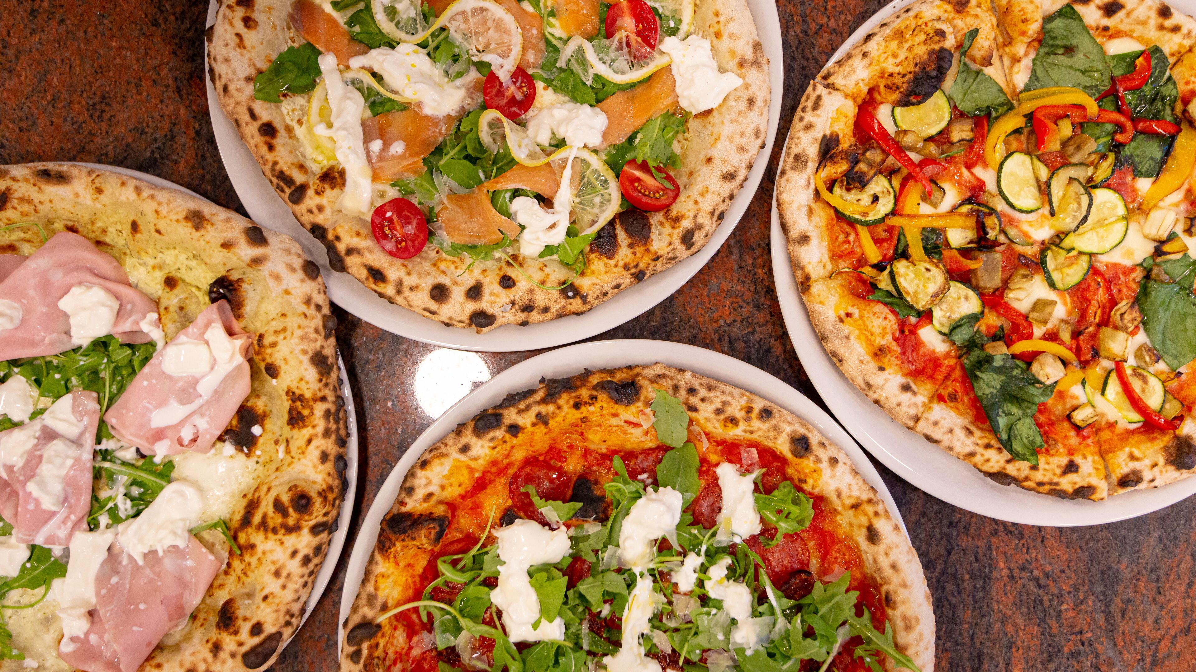 Fünf Pizzen mit unterschiedlichen Belägen auf einem Tisch.