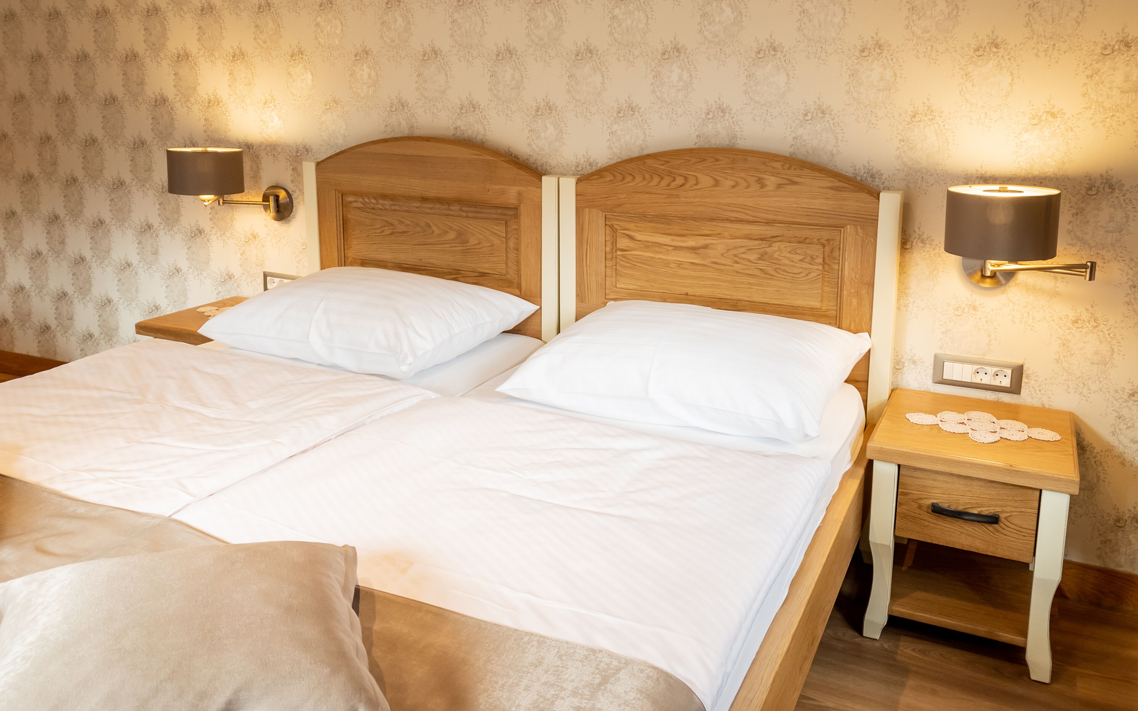 Una cama doble con ropa de cama blanca, dos mesitas de noche con lámparas y una mesita con toma de corriente.
