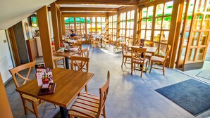 A restaurant with wooden tables and chairs, large windows, and a tiled floor. - Guest House Pri Cesarju (Kamnik)