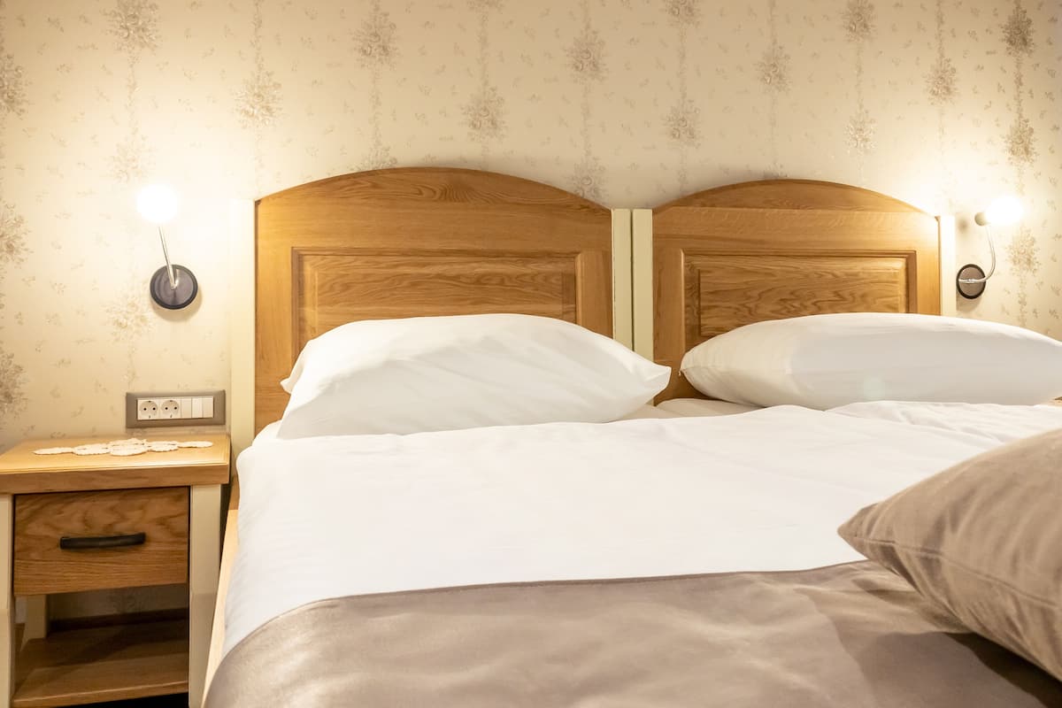 A double bed with wooden headboard and nightstands, a wall socket, and a small table with a lamp.