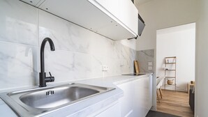 Moderni keittiö, jossa on valkoiset marmorilaatat, ruostumattomasta teräksestä valmistettu allas ja valkoiset kaapit.