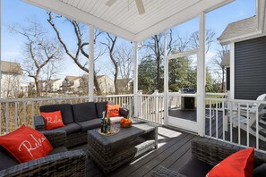 A covered outdoor deck with a sofa, cushions, and a table set with bottles and oranges.